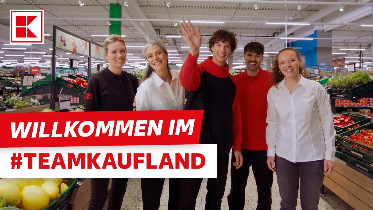 Fünf lächelnde Mitarbeiter und Mitarbeiterinnen von Kaufland stehen in einer Filiale. Der Text "WILLKOMMEN IM #TEAMKAUFLAND" ist eingeblendet.